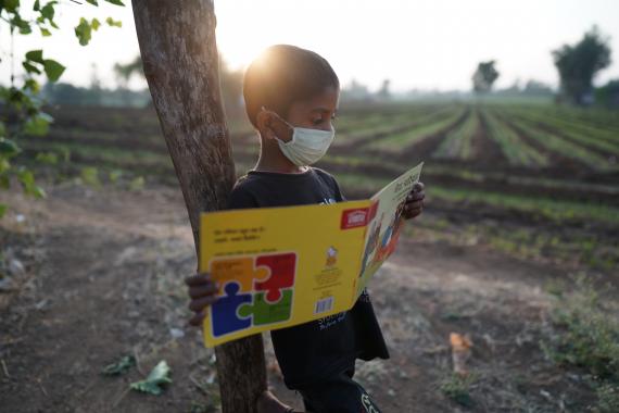 8 year old Akash reads a pratham book outside his house that has been given to him under the library program of Room to Read