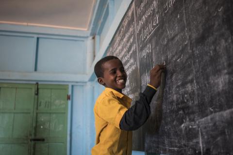 A student laughs as he writes the answers to questions on the chalkboard of his classroom.